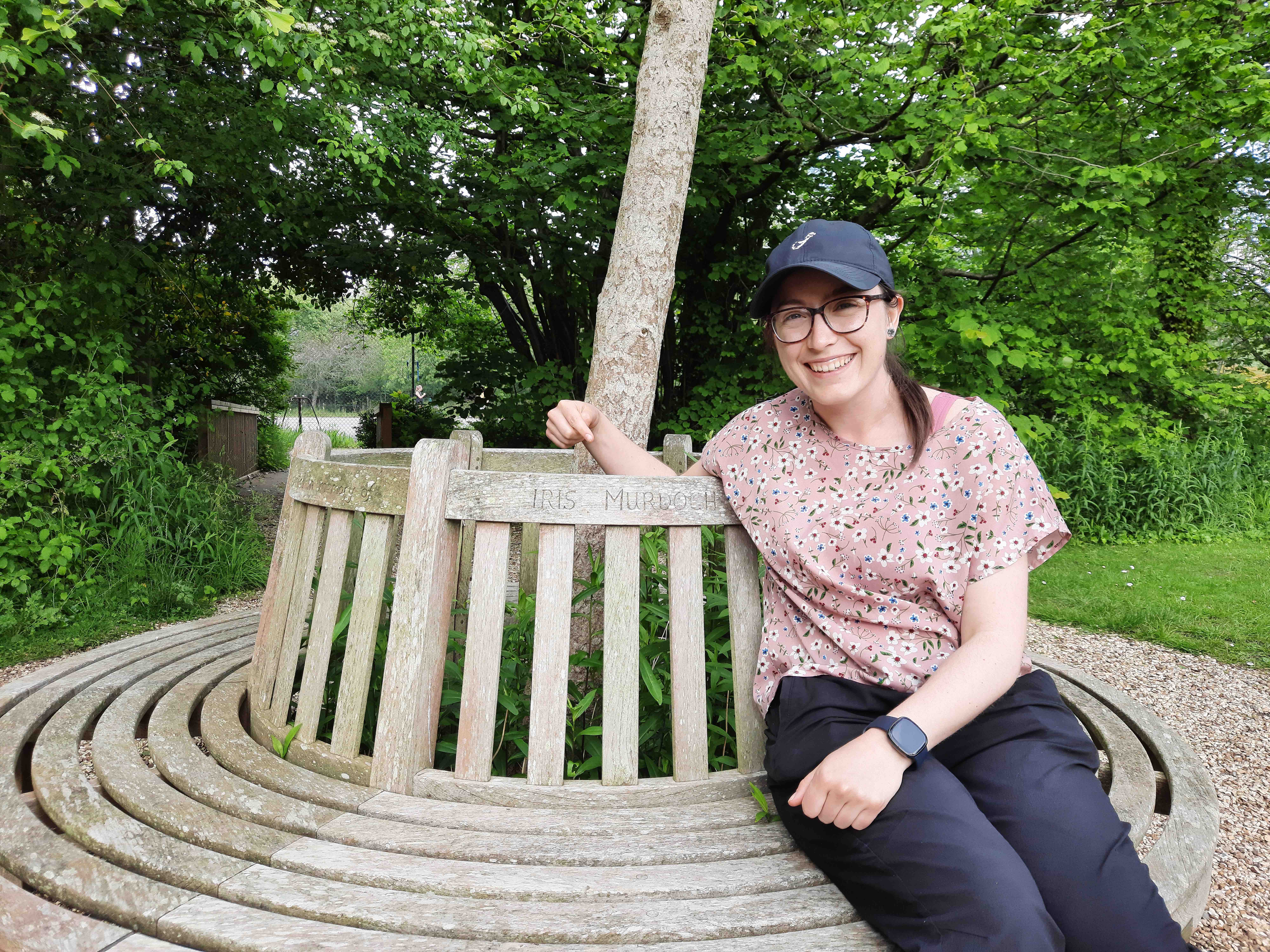 Amy Ward sitting on a bench dedicated to Iris Murdoch in Oxford